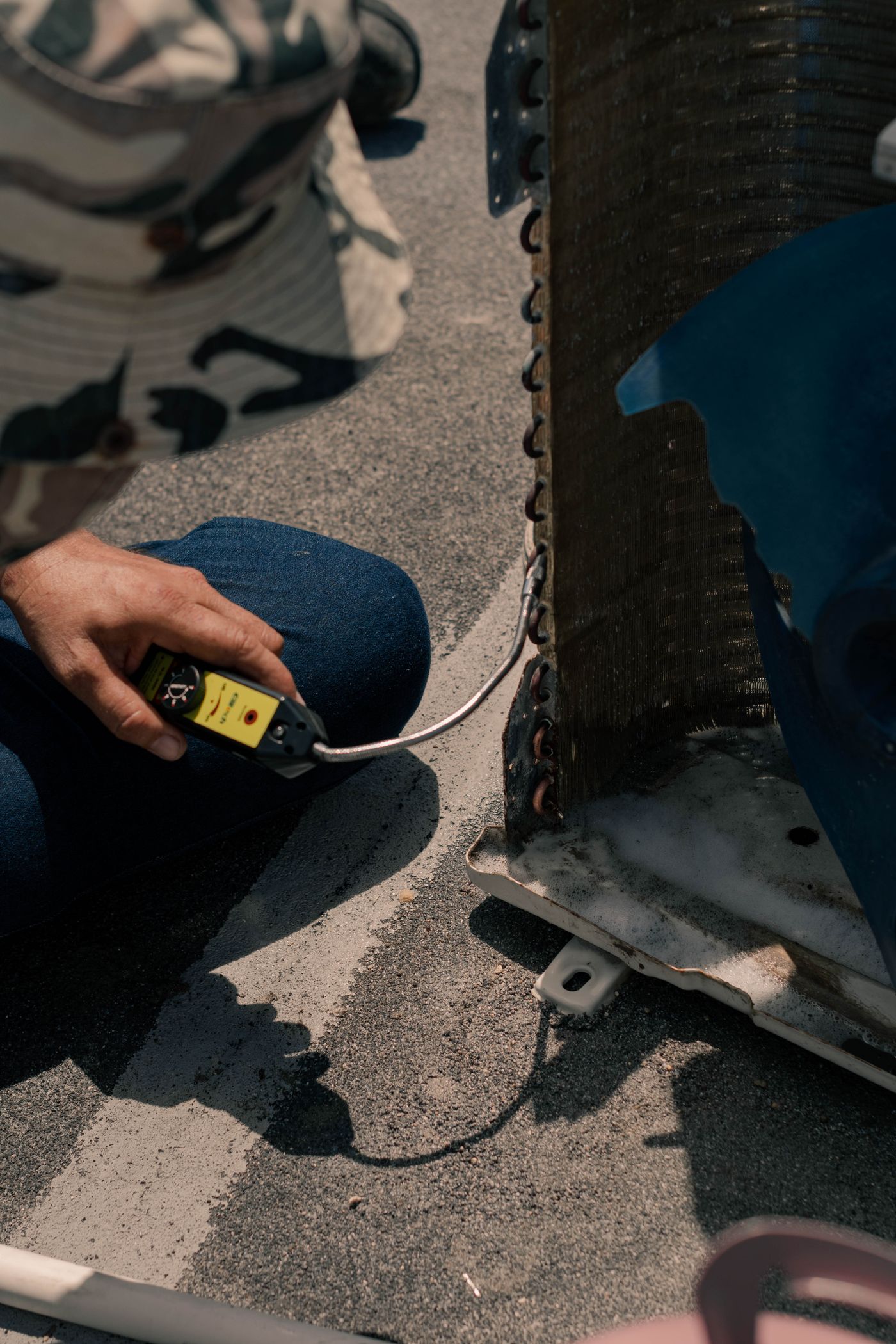 A technician holding an electronic refrigerant leak detector against the coil of an outdoor air conditioning unit.
